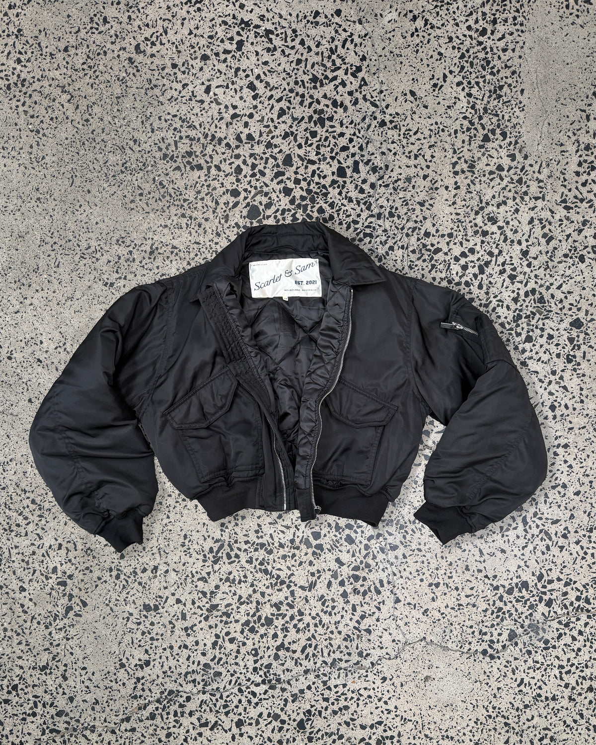 Black Capsule Bomber, laid flat, showing the collar and front pockets.