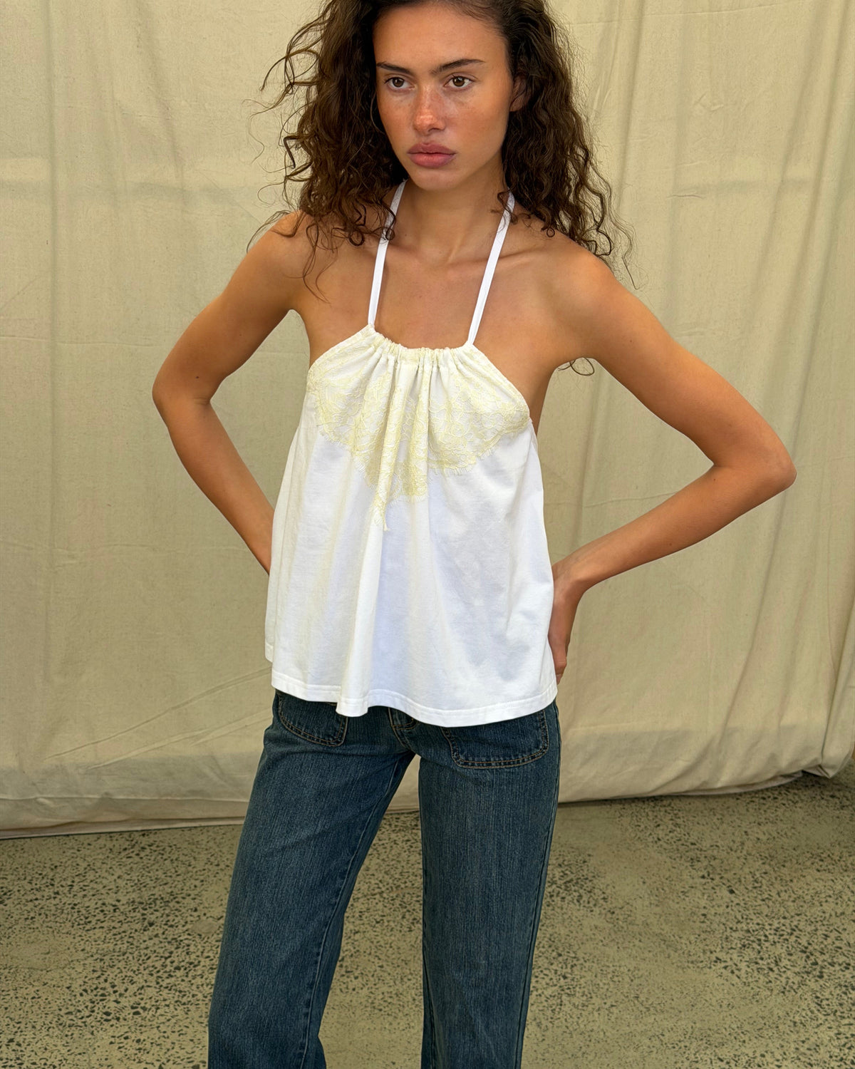 model:XS/6AU
Front view of the white Jersey Lace Halter Top with cream lace detailing, gathered neckline and a loose hem, worn with blue jeans.