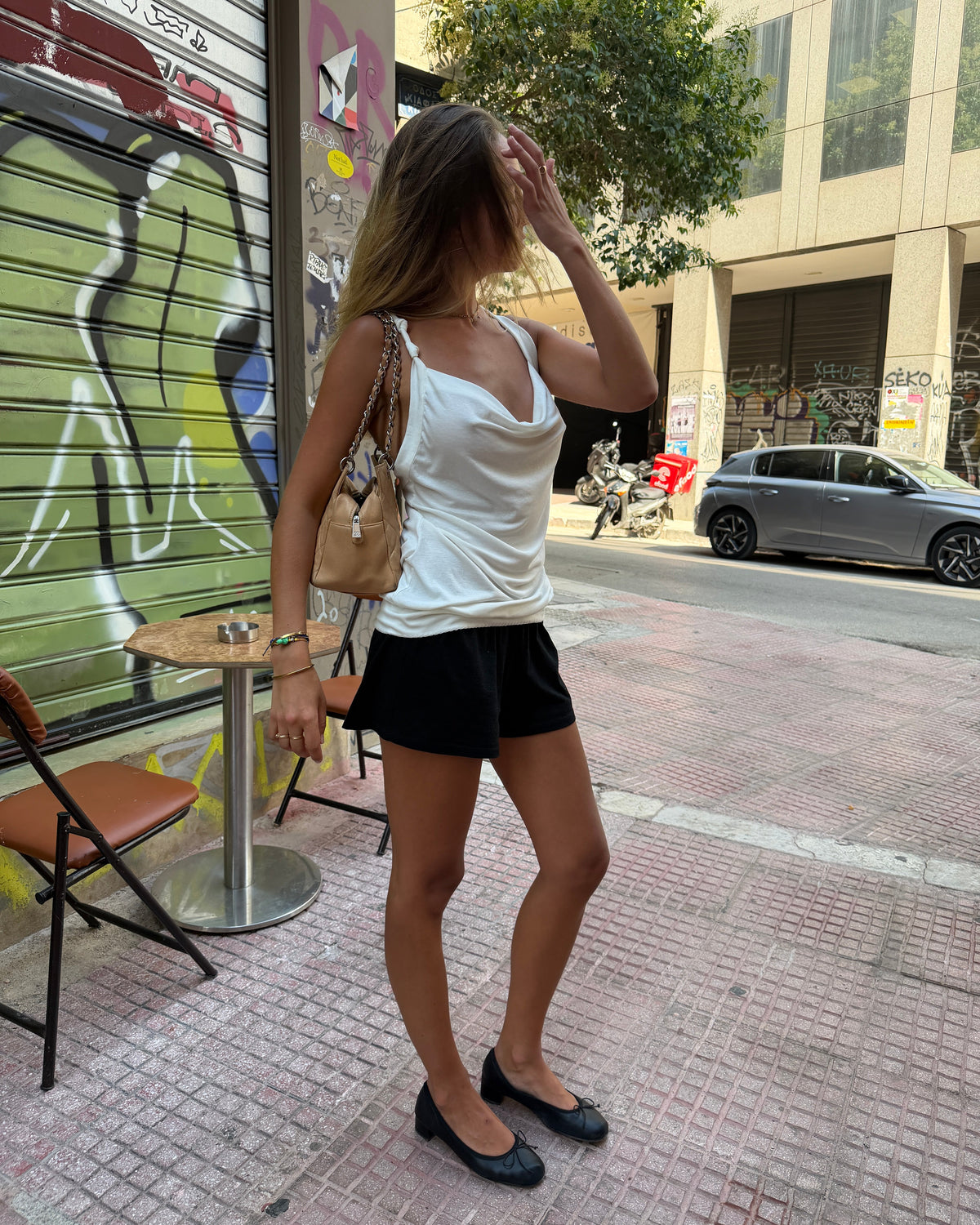 model:S/8AU H:173CM 
White Cowl Knot Tank worn on a city street with black shorts and ballet flats, showing its draped neckline and longline hem.