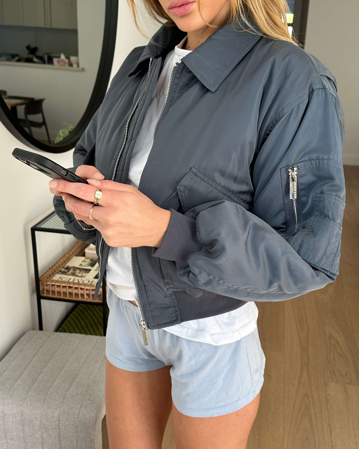 model:S/M/6-10AU H:171CM 
Charcoal Capsule Bomber, worn open over a white top and pale blue shorts.