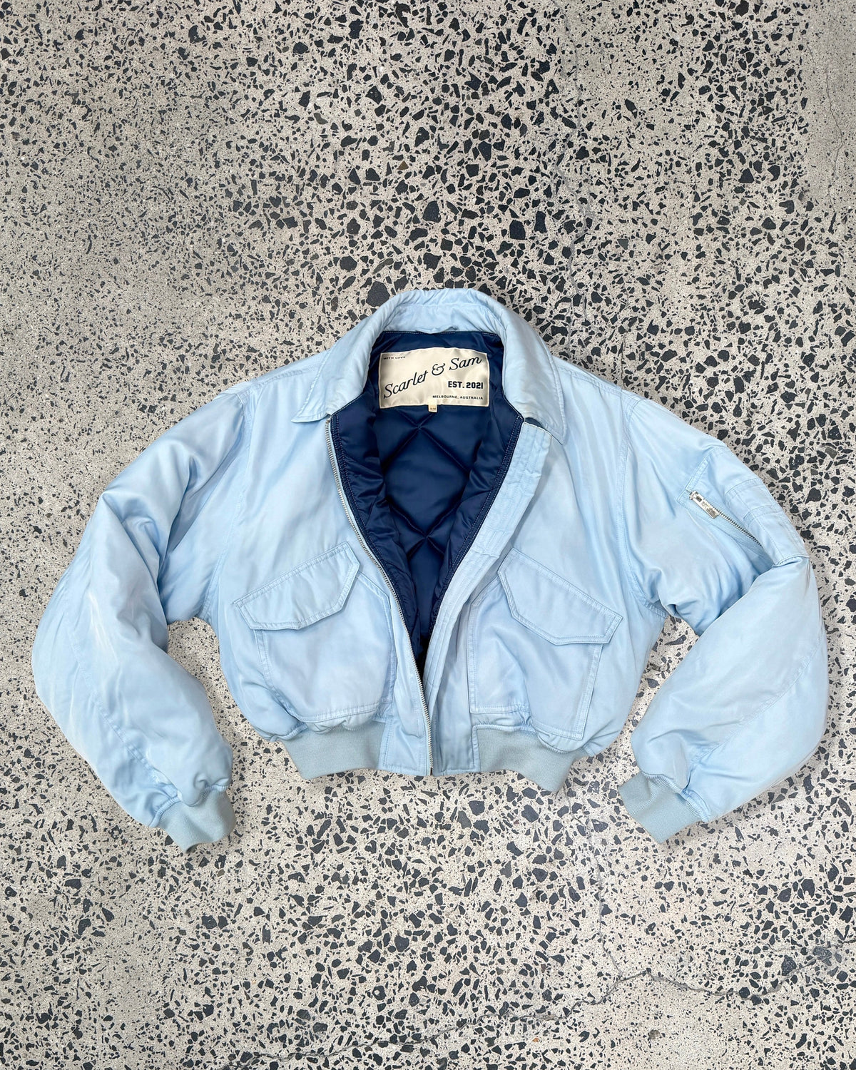 Baby Blue Capsule Bomber, laid flat with dark blue lining visible.