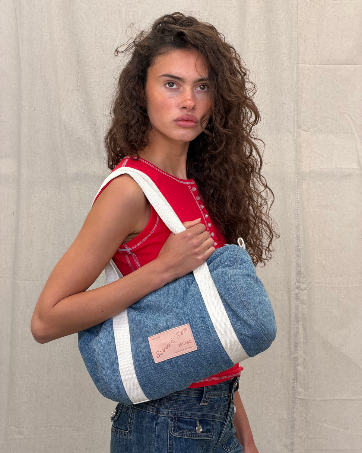 Denim Padded Barrel Tote, angled front view worn over the shoulder, showing cream canvas handles and logo patch.