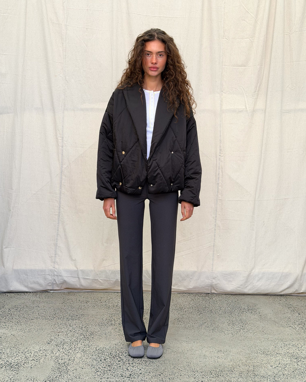 model:S/6-8AU H:179CM 
Black Cocoon Padded Jacket, full-length front view, worn open over a white top with charcoal trousers and grey ballet flats.