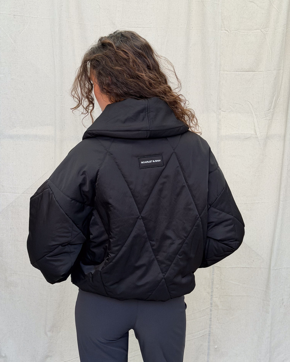 model:XS/6AU H:179CM 
Black Cocoon Padded Jacket, back view, showing the diamond quilting, oversized collar and Scarlet & Sam patch.