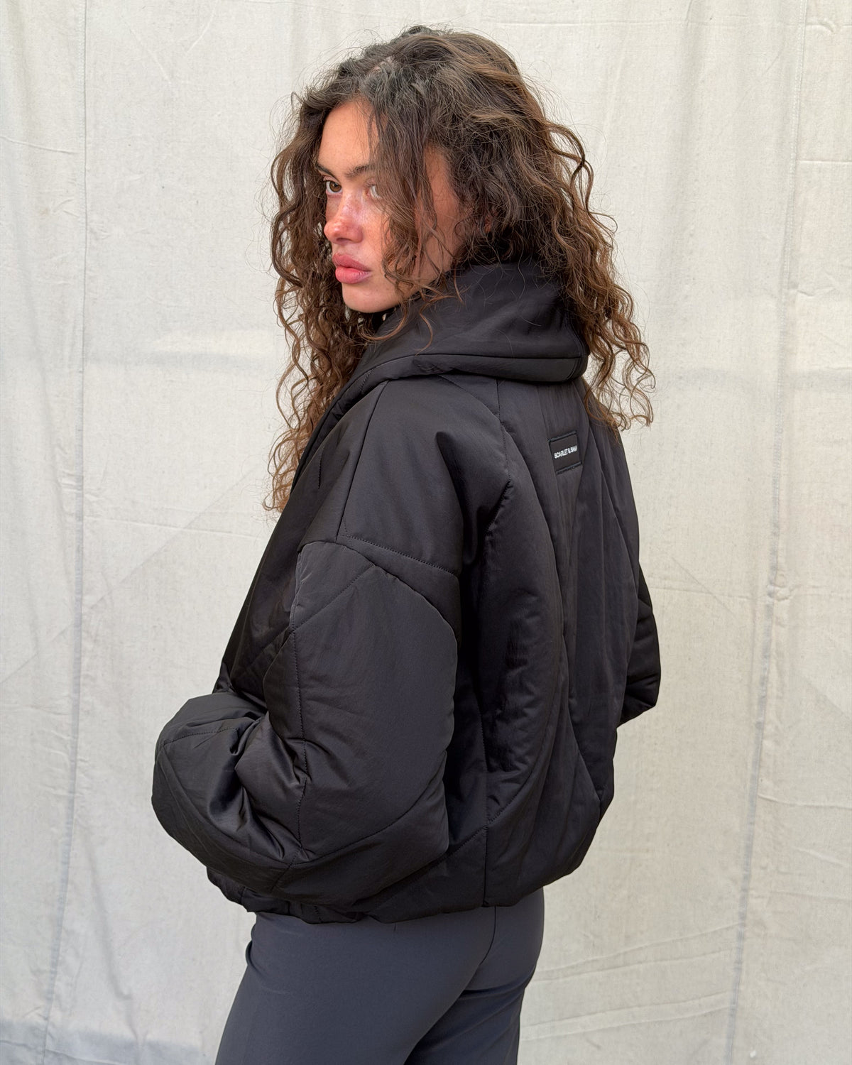 model:XS/6AU H:179CM 
Black Cocoon Padded Jacket, angled back view, showing the padded collar, dropped shoulder and quilted sleeve.
