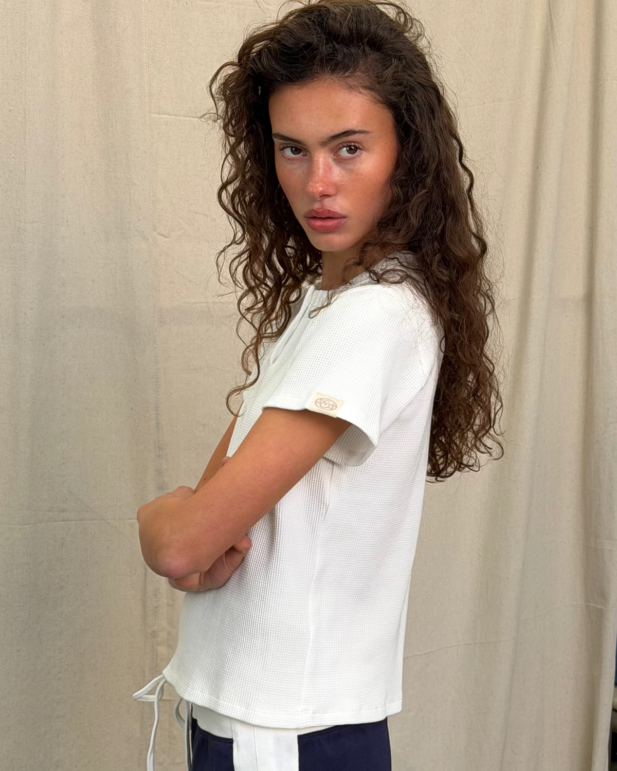 model:S/8AU H:179CM 
Scarlet & Sam white Waffle Tee, side view on a model with folded arms, showing the relaxed fit and sleeve logo tab.