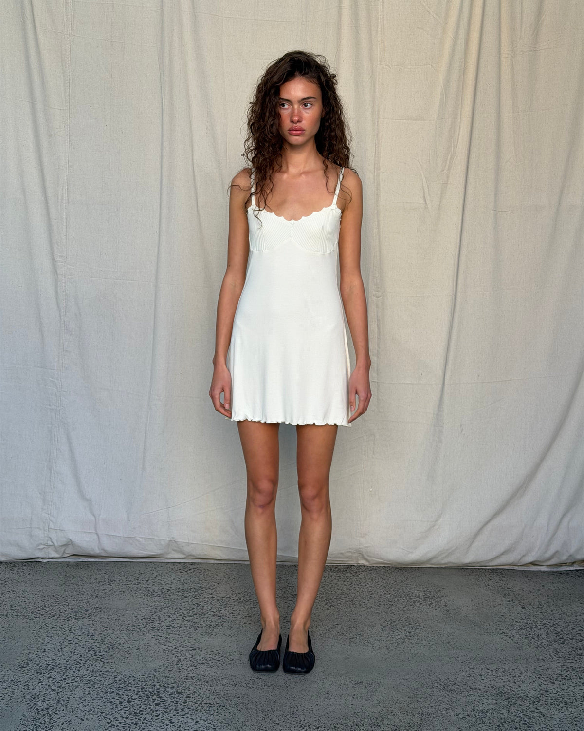 model:XS/6AU
Full-length front view of the cream Ribbed Knit Dress with slim straps and a scalloped mini hem, styled with black flats.