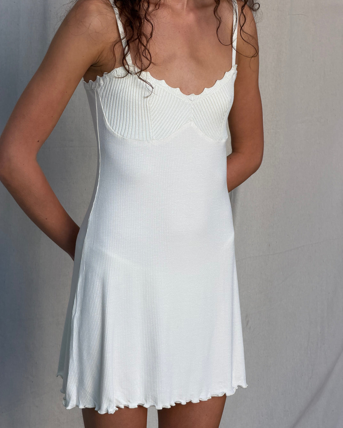 model:XS/6AU
Detail of the cream Ribbed Knit Dress, showing the shaped knitted bust, scalloped neckline, fine ribbing and wavy mini hem.