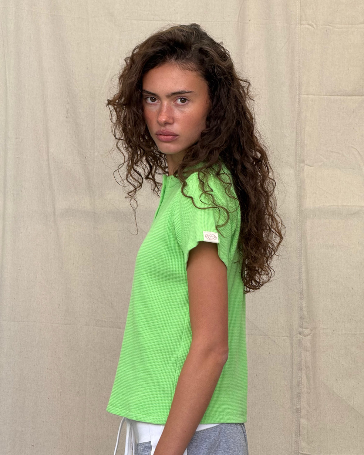 model:S/8AU H:179CM 
Scarlet & Sam apple green Waffle Tee, side view on a model looking towards the camera, showing the relaxed fit and sleeve tab.