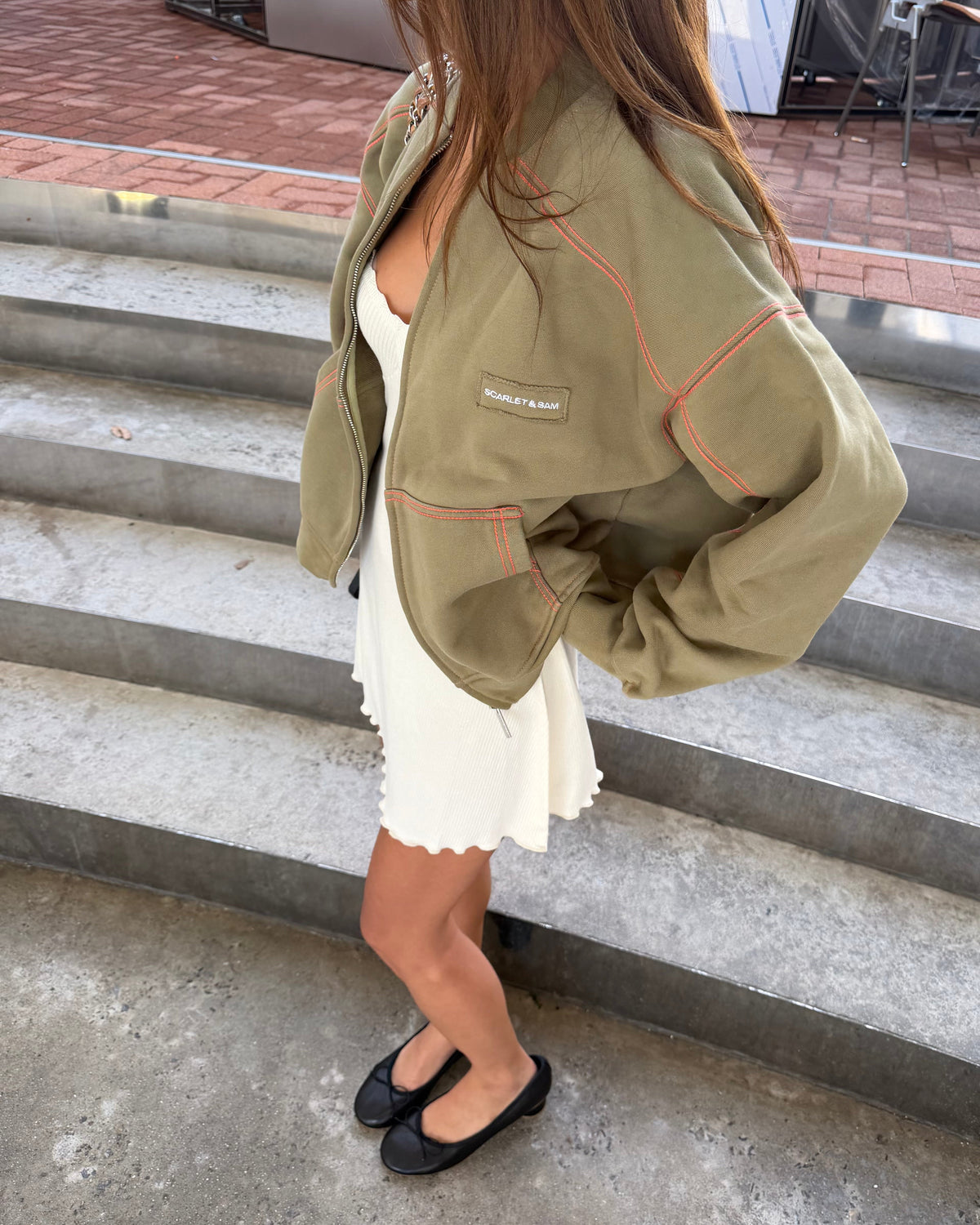 model:S/6-8AU
Side view of the khaki Capsule Stitch Cardigan worn open over a cream dress, highlighting the relaxed fit, contrast seams and front pocket.