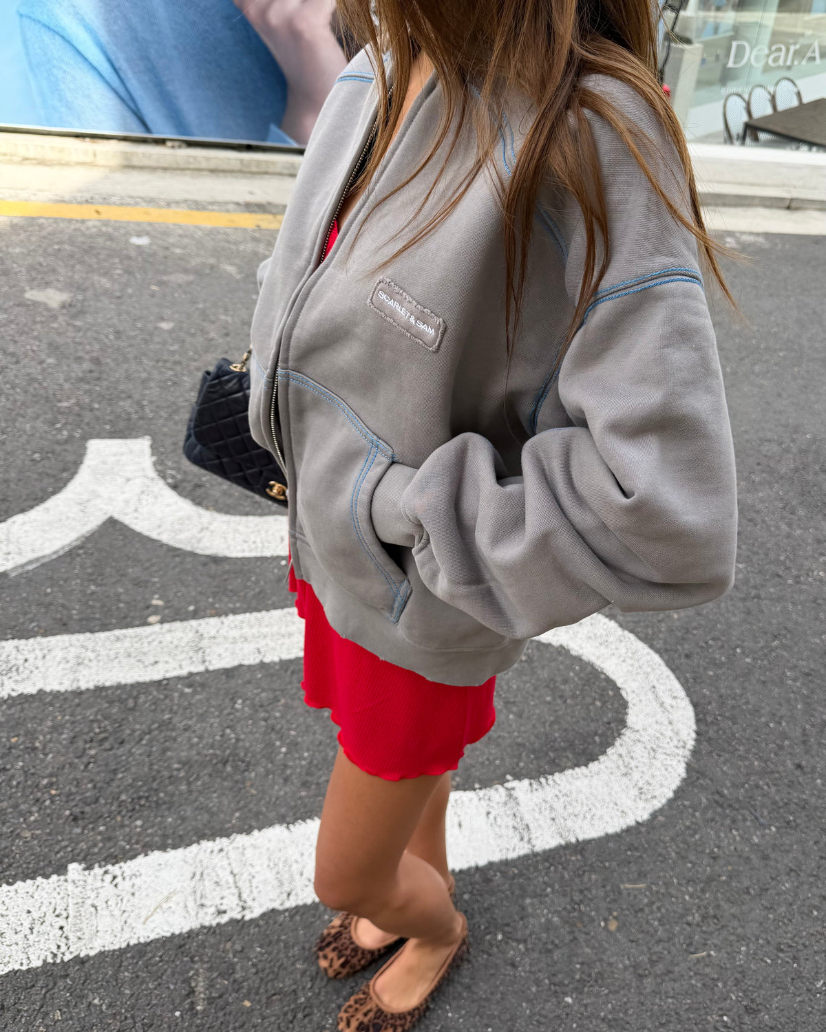 model:S/6-8AU
Side view of the grey Capsule Stitch Cardigan over a red dress, showing its relaxed sleeves, blue contrast stitching and front pocket.