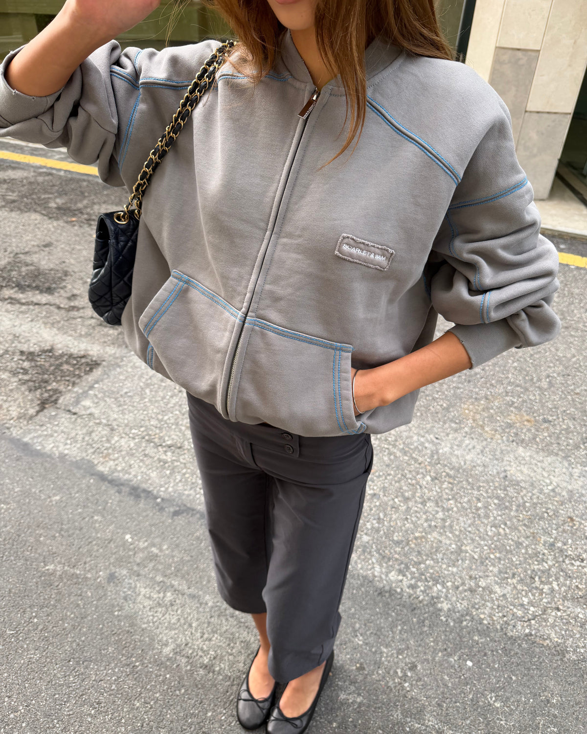 model:S/6-8AU
Grey Capsule Stitch Cardigan worn zipped with sleeves pushed up, showing blue contrast seams, front pockets and the Scarlet & Sam logo patch.